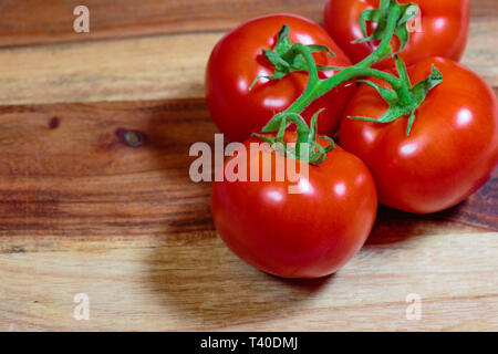 Four tomatoes on a green vine laying on a cuttung board Stock Photo