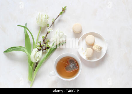 Spring blossoms and a cup of tea with a heart shape tea bag and macaroons on a bright background, flat lay style with a copy space Stock Photo
