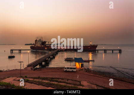 Port operations for managing and transporting iron ore at dawn. TSV ship unberthing from layby jetty to move and load at loading jetty. Sierra Leone Stock Photo