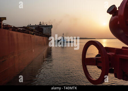Sunrise during port operations managing and transporting iron ore. Ship to ship moving and berthing operation from tug to leading tug prior to sailing Stock Photo