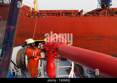 Port operations managing and transporting iron ore. Unberthing loaded transhipper from jetty before it leaves to meet OGV ship at sea by tug crewman. Stock Photo