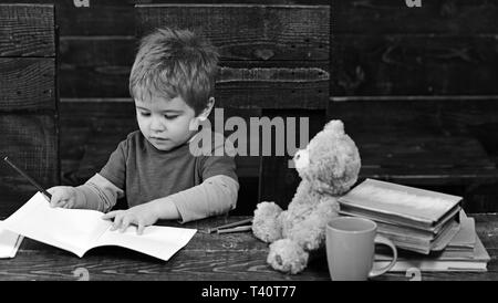 Concentrated kid writing in copybook. Preschool boy sitting at desk. Learning letters in kindergarten Stock Photo
