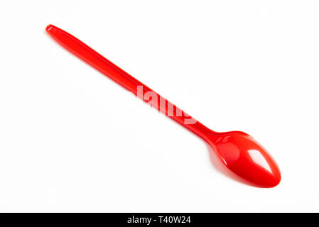 A red shiny long plastic spoon artistically set on a plain white background with negative spaces. Stock Photo