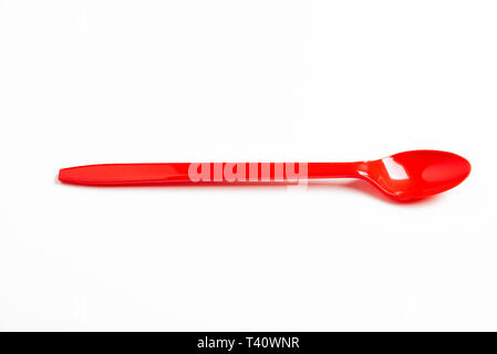 A red shiny long plastic spoon artistically set on a plain white background with negative spaces. Stock Photo