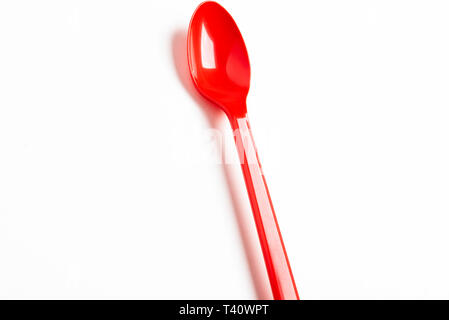 A red shiny long plastic spoon artistically set on a plain white background with negative spaces. Stock Photo