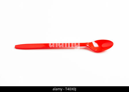 A red shiny long plastic spoon artistically set on a plain white background with negative spaces. Stock Photo