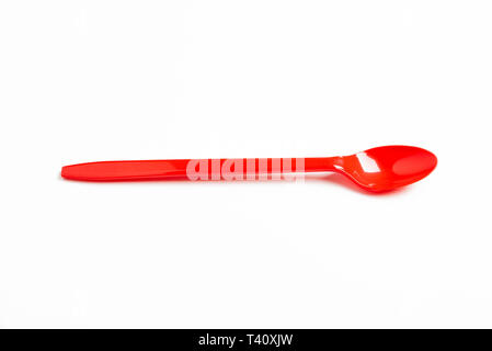 A red shiny long plastic spoon artistically set on a plain white background with negative spaces. Stock Photo