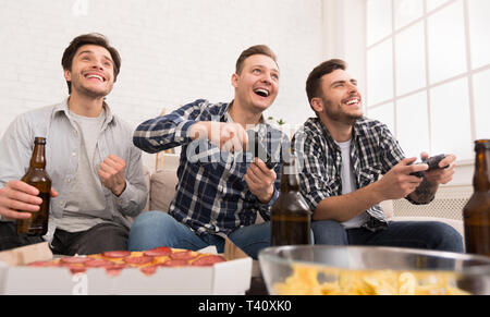 Excited men playing video game, having home party Stock Photo
