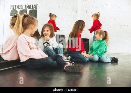 The kids sitting at dance school. Ballet, hiphop, street, funky and modern dancers concept. Studio background. Teens in hip hop style. Sport, fitness and lifestyle concept. Stock Photo