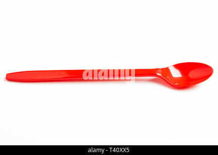 A red shiny long plastic spoon artistically set on a plain white background with negative spaces. Stock Photo