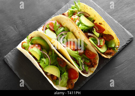 Tacos with meat and vegetables on slate board over black stone background. Stock Photo