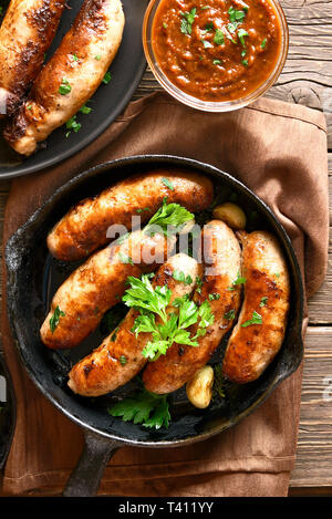 Homemade grilled sausages in frying pan and tomato sauce on wooden table. Top view, flat lay Stock Photo