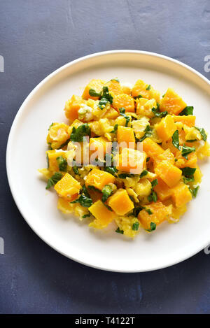Pumpkin and egg stir fry in thai style. Stir-fried pumpkin with eggs on plate over blue stone background. Stock Photo