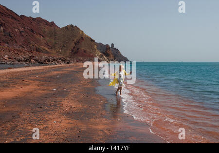 Woman walking in the surf on Red beach, Hormuz, Hormozgan Province, Southern Iran Stock Photo