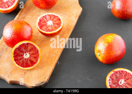 Whole and halved blood oranges on black surface, side view. Stock Photo