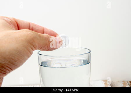 Hand throws an effervescent tablet into a glass of water against a white background Stock Photo