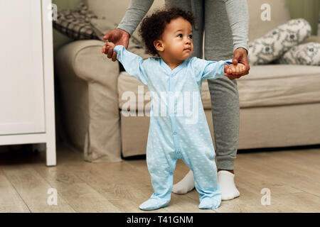 Mother teaching baby boy to walk in a room. Woman holding hands of her son. Stock Photo