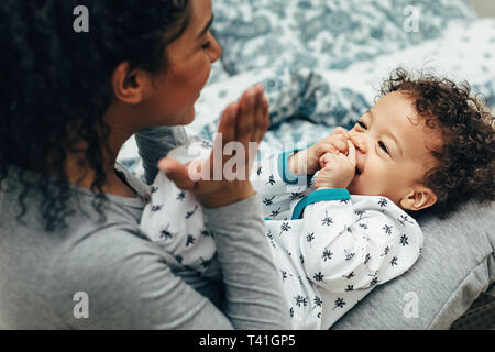 Happy baby boy lying on mother legs while she playing with him Stock Photo