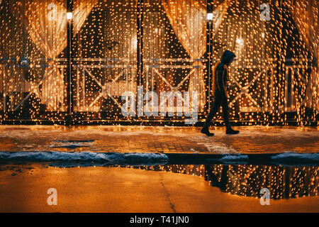 Young man walking on illuminated city street at night during winter Stock Photo