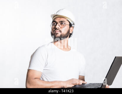 Young builder engineer in glasses and a white safety helmet, stands with an open laptop Stock Photo
