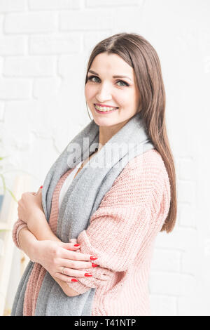 Portrait of a beautiful young brunette woman in a sweater with a scarf on a light background Stock Photo