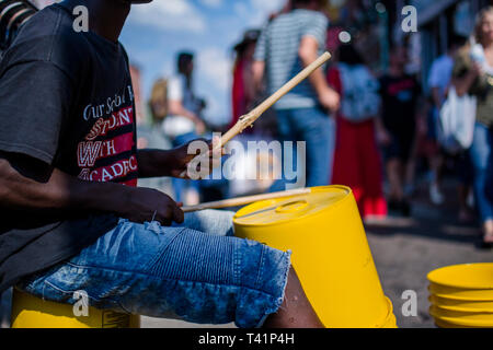 a teenager plays drums on a bucket along a crowded street Stock Photo