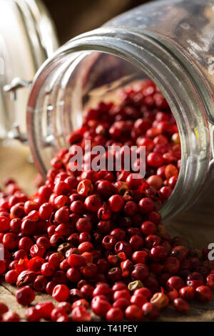 Pink or rose brazilian red peppercorns (schinus terebinthifolius) in glass jar on rustic wooden table background - selective focus Stock Photo