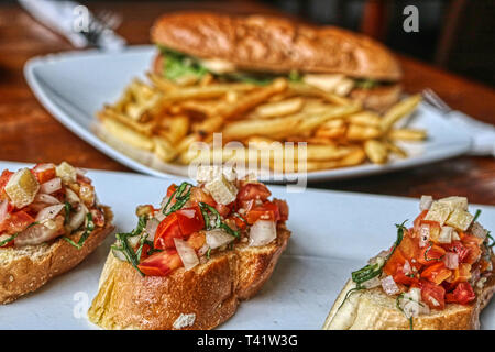 In the foreground, this unique photo shows the bruschetta appetizer and in the background you can see a cheese sandwich with chips Stock Photo