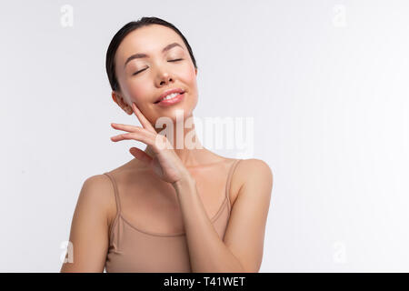Eyes closed. Dark-haired woman wearing beige camisole closing her eyes feeling truly satisfied Stock Photo