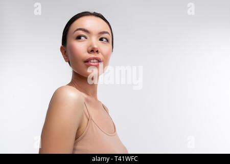Woman near background. Dark-eyed beautiful woman wearing beige camisole standing near white background Stock Photo