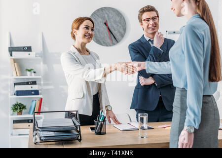cropped view of woman shaking hands with cheerful recruiter near handsome coworker in glasses Stock Photo