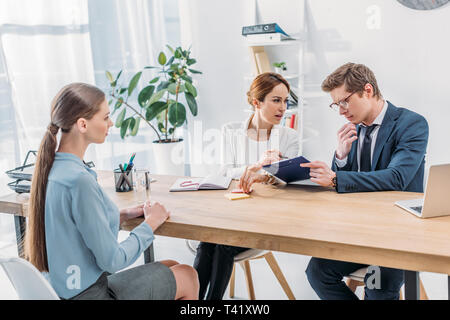 handsome recruiter in glasses holding clipboard near woman while speaking near attractive employee Stock Photo