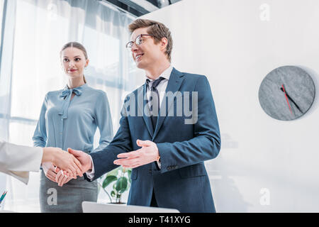 low angle view of cheerful recruiter shaking hands with woman near attractive colleague in office Stock Photo