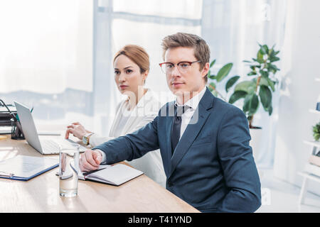 handsome recruiter in glasses sitting with attractive coworker in office Stock Photo