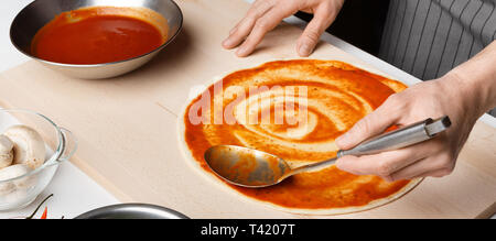 Chef spreading tomato paste on pizza base Stock Photo