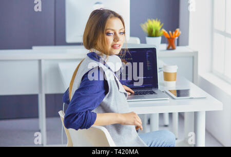 Focused attentive woman in headphones sits at desk with laptop, looks at screen, makes notes, learns foreign language in internet. Stock Photo