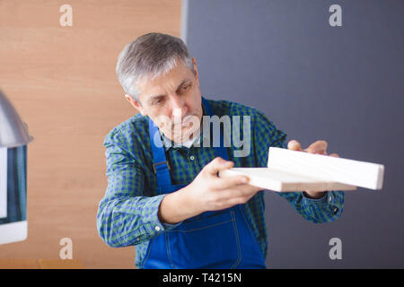 profession, carpentry, woodwork and people concept - carpenter testing wood plank evenness at workshop. Stock Photo