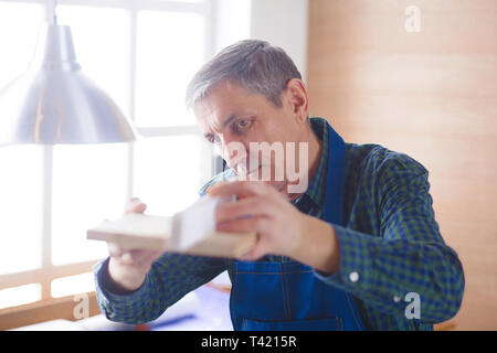profession, carpentry, woodwork and people concept - carpenter testing wood plank evenness at workshop. Stock Photo