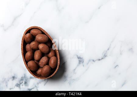 Chocolate easter egg filled with mini eggs on a marble background Stock Photo