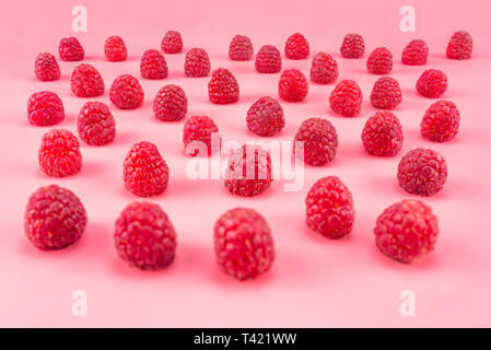 Pattern made from fresh raspberries, view from the skew, isolated on a light pink background. Stock Photo