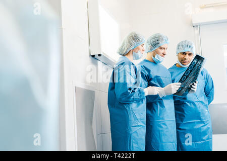 selective focus of handsome and attractive doctors in uniforms and medical masks talking about x-ray Stock Photo