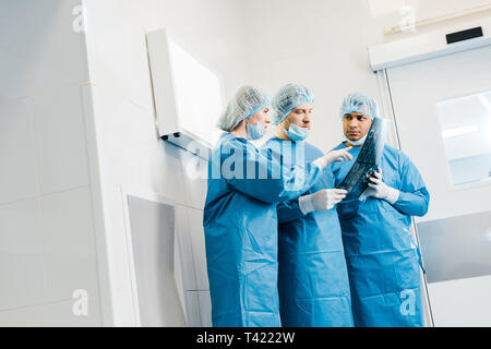 handsome and attractive doctors in uniforms and medical masks pointing with finger at x-ray and talking Stock Photo