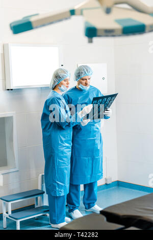 handsome and beautiful doctors in uniforms holding x-ray and talking in clinic Stock Photo