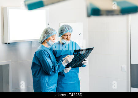 selective focus of handsome and beautiful doctors in uniforms holding x-ray and talking Stock Photo