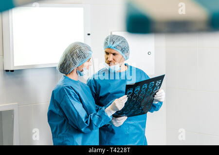 selective focus of handsome and beautiful doctors in uniforms holding x-ray and talking Stock Photo