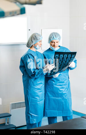 handsome and beautiful doctors in uniforms holding x-ray and talking in clinic Stock Photo