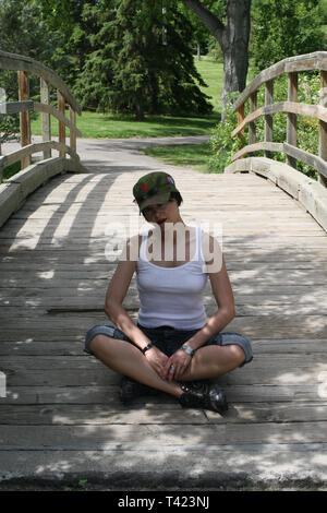 Dark haired beautiful woman posing In a park and sitting on a bridge Stock Photo