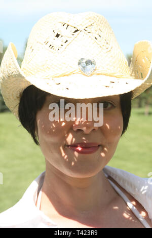 Dark haired beautiful woman posing In a park wearing a straw hat Stock Photo