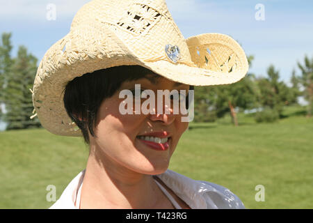 Dark haired beautiful woman posing In a park wearing a straw hat Stock Photo