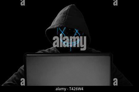 hacker with glowing mask behind notebook laptop in front of isolated black background internet cyber hack attack computer concept Stock Photo